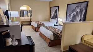 Habitación de hotel con dos camas, un escritorio con cafetera, un cubo de basura y cuadros en la pared.