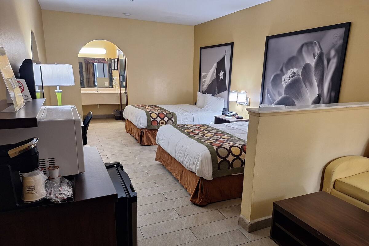 A hotel room with two beds, a desk with a coffee machine, a trash bin, and framed pictures on the wall.