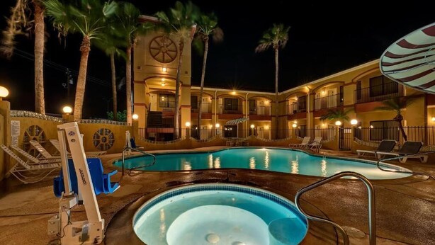 Un hotel con piscina, sillas de descanso y palmeras.