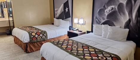 A hotel room with two beds, each with a patterned bedspread and a brown skirted bed base. There is a nightstand with a phone and a lamp between the beds. The walls are beige, and there are two large framed pictures above the beds.