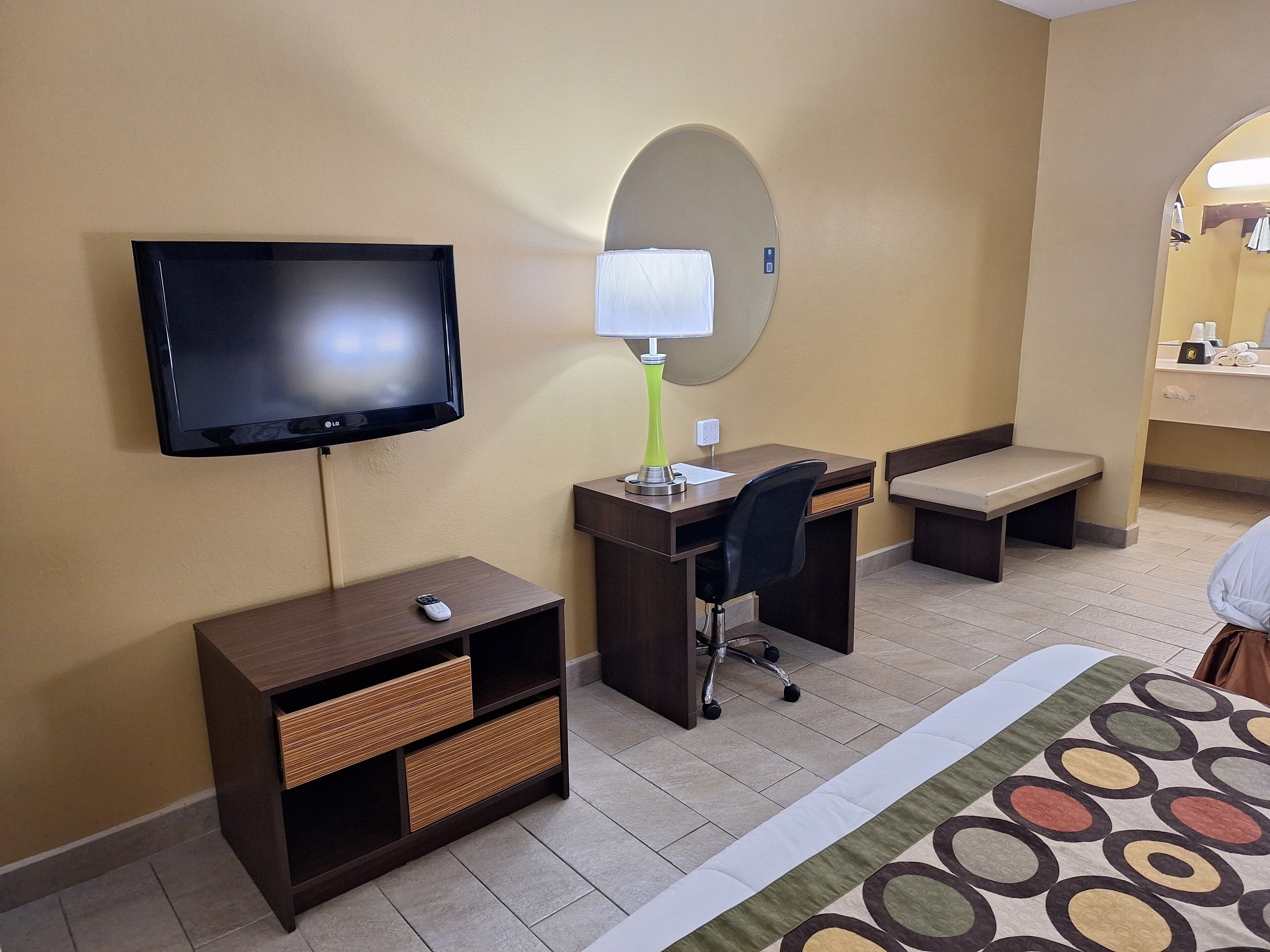Een hotelkamer met een flatscreen televisie, een bureau met lamp, een stoel, een bankje en een bed met een gestreept beddegoed.