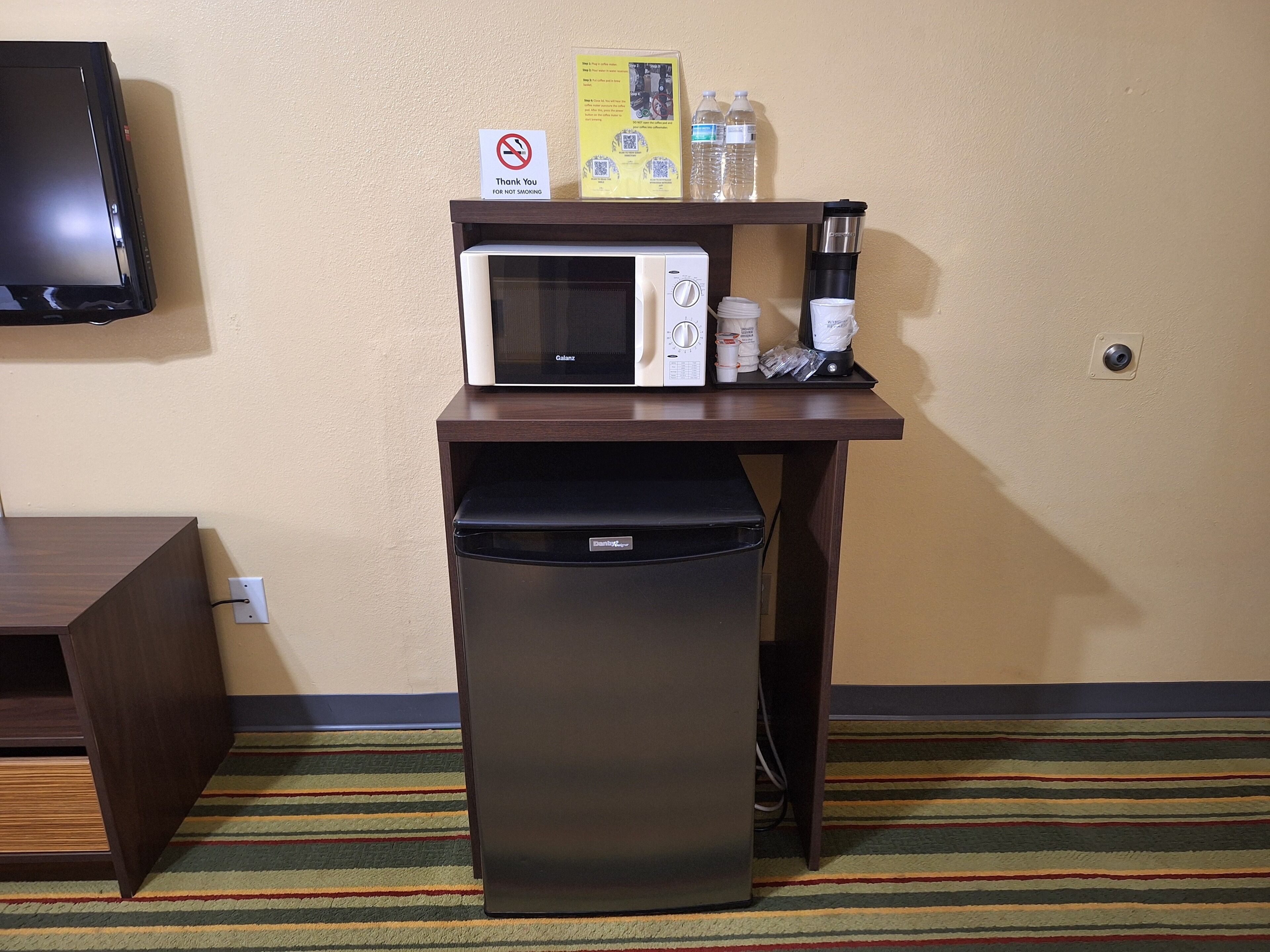 A compact kitchenette with a microwave, coffee maker, and a trash bin.