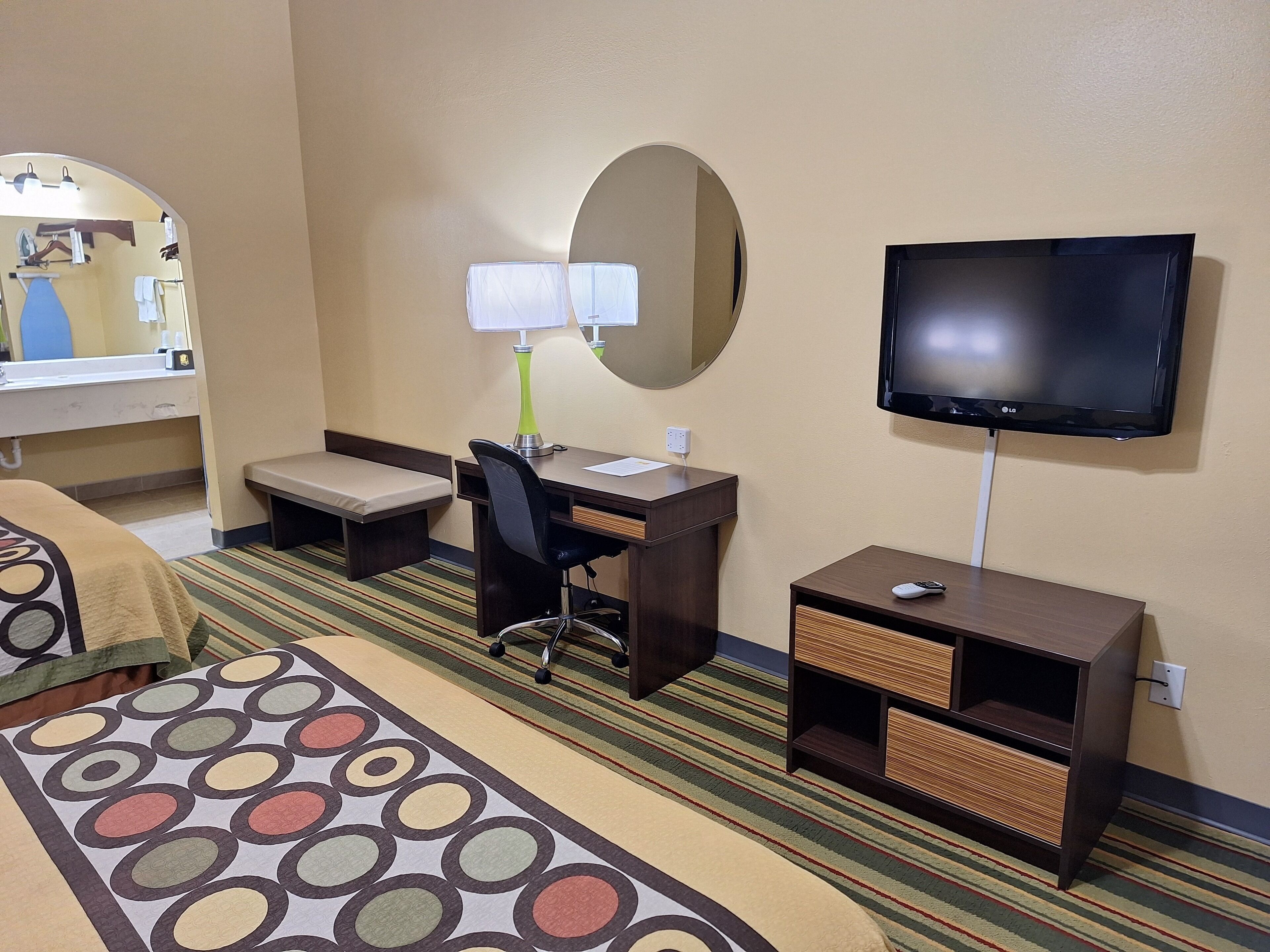 Una habitación de hotel con cama, escritorio, silla, televisor y una mesita.