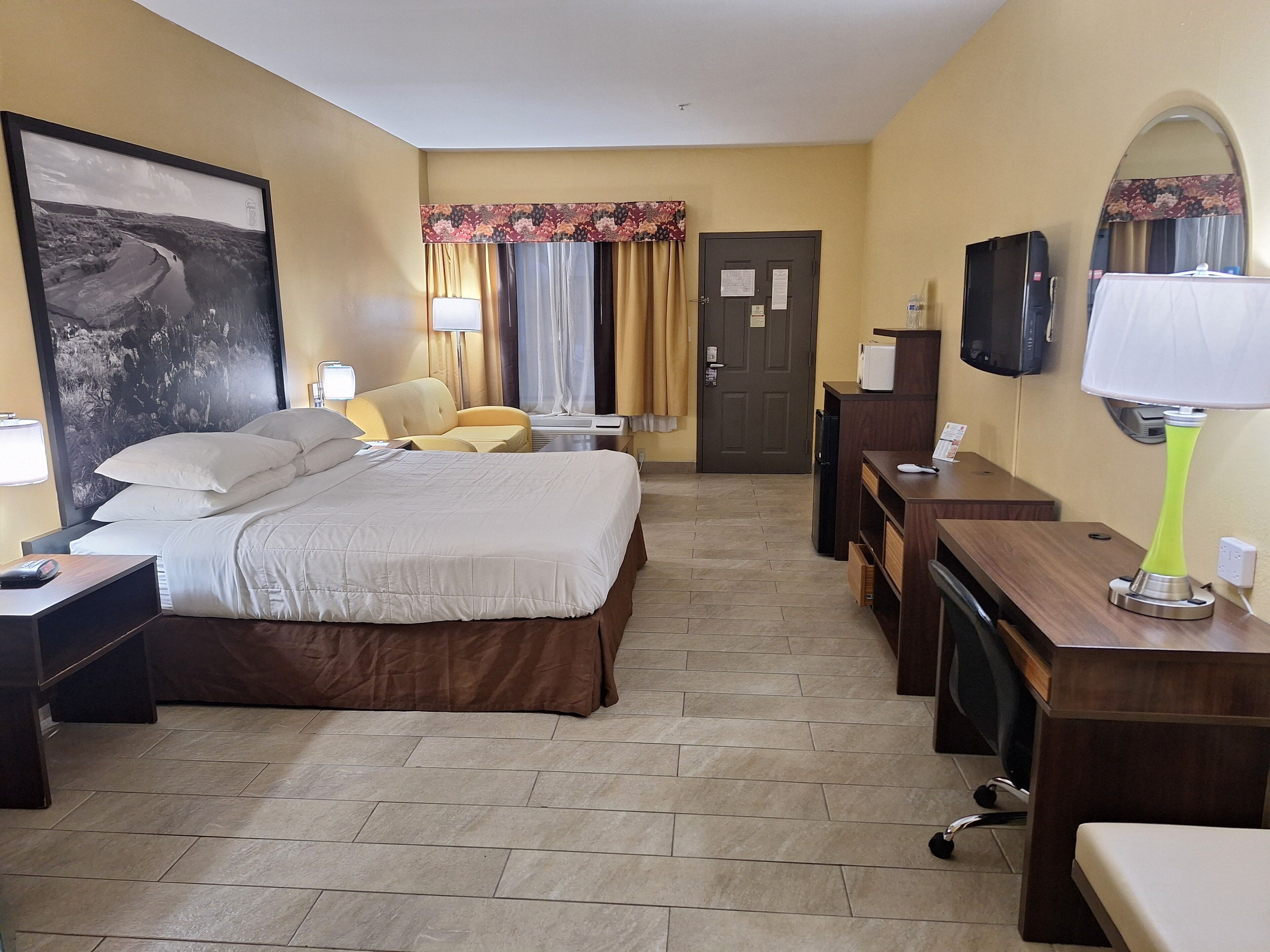 Une chambre d’hôtel avec un lit, un bureau, une chaise, un téléviseur et un grand tableau encadré au mur.