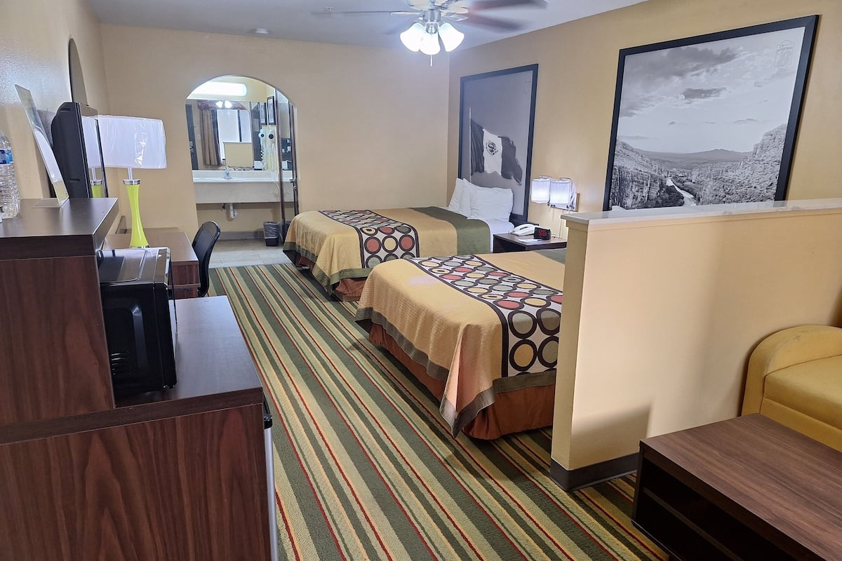 A hotel room with two beds, a desk, a chair, a mirror, and a ceiling fan.