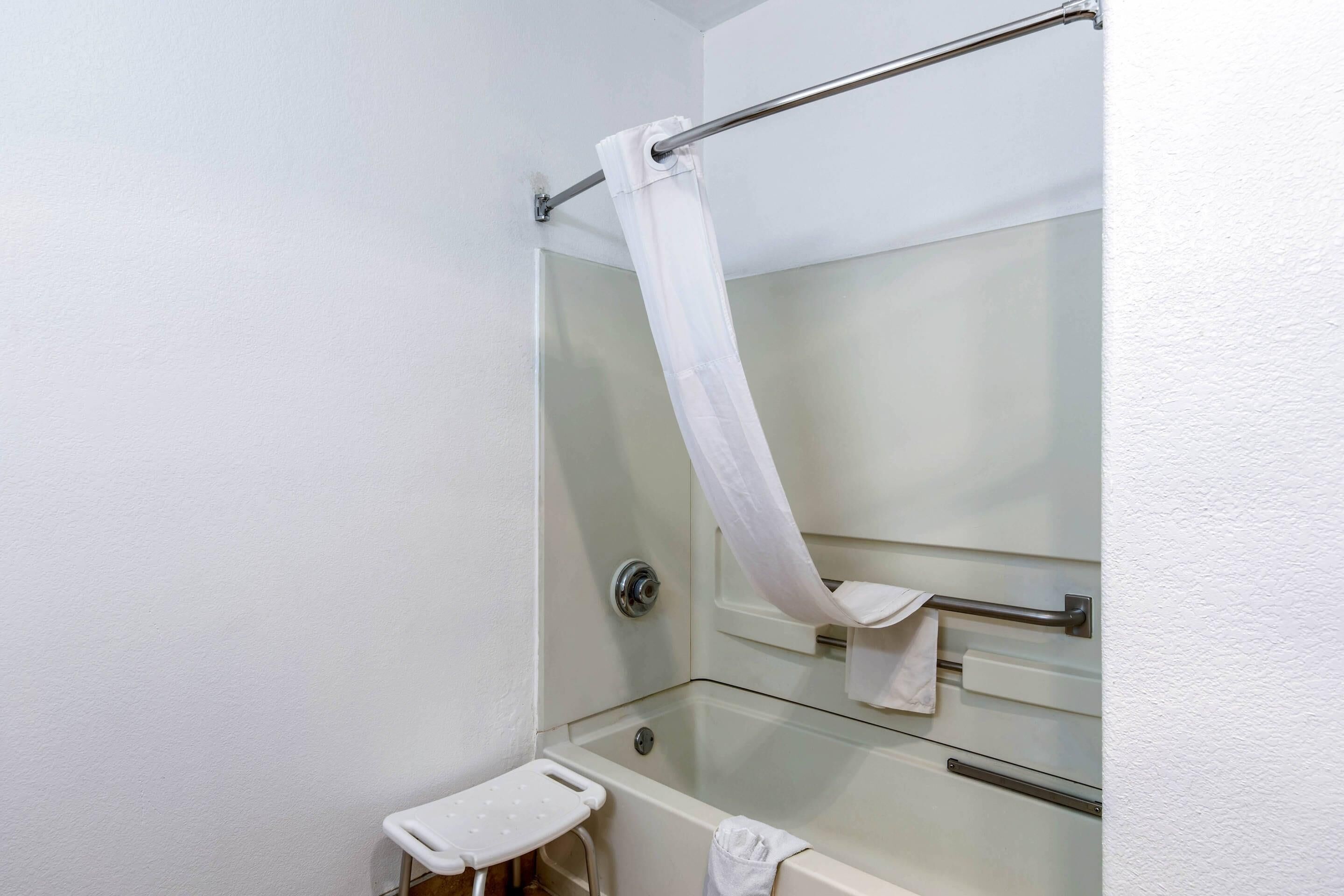 A bathroom with a glass-enclosed shower, a white towel rack, and a small white stool.