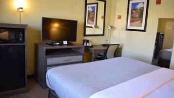 Habitación de hotel con cama, televisión, escritorio con lámpara, microondas y refrigerador.