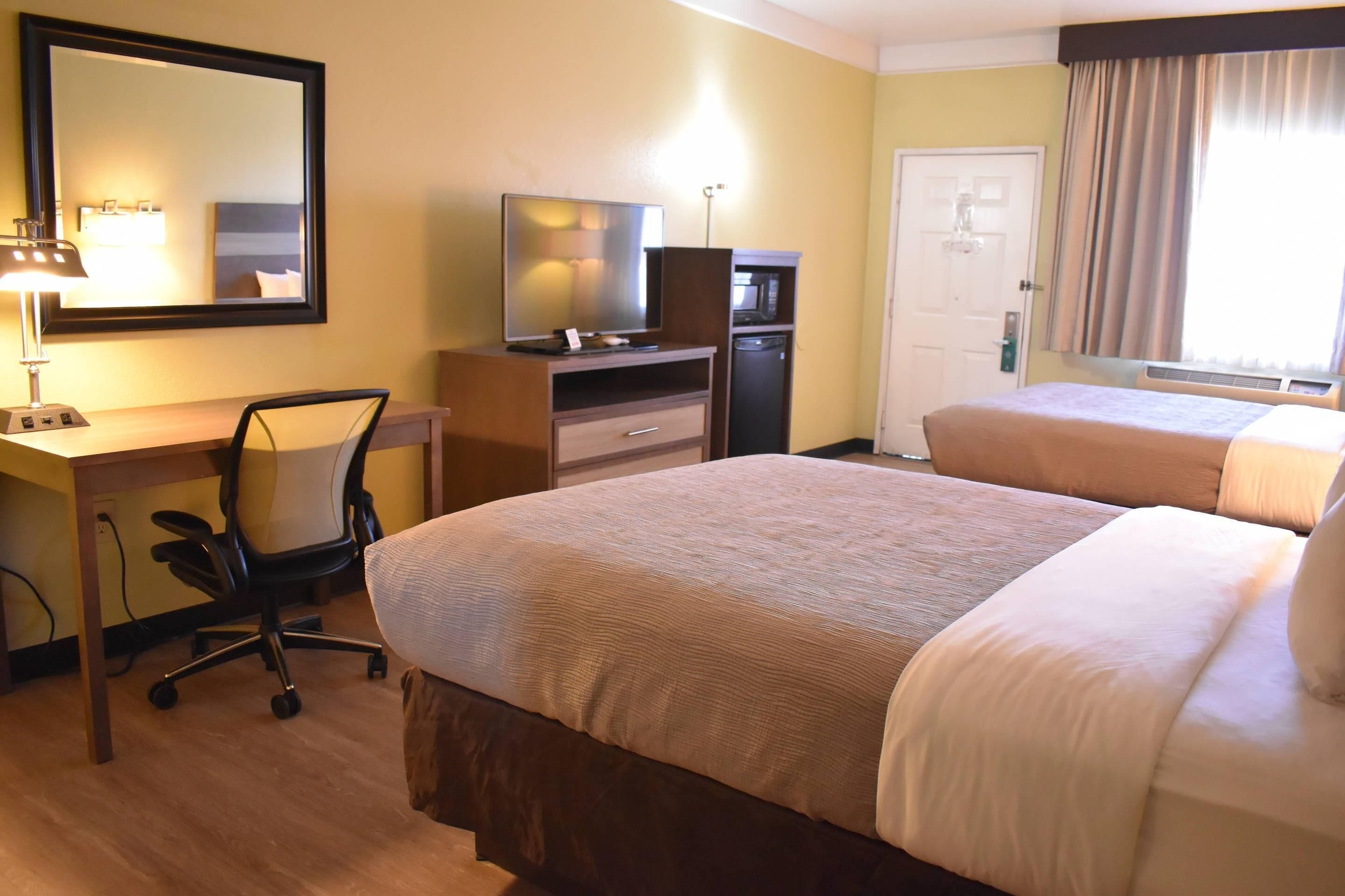 A hotel room with a desk, chair, two beds, a mirror, a television, and a microwave.