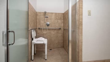 A glass-enclosed shower stall with a white chair, a handheld showerhead, and a wall-mounted control panel.