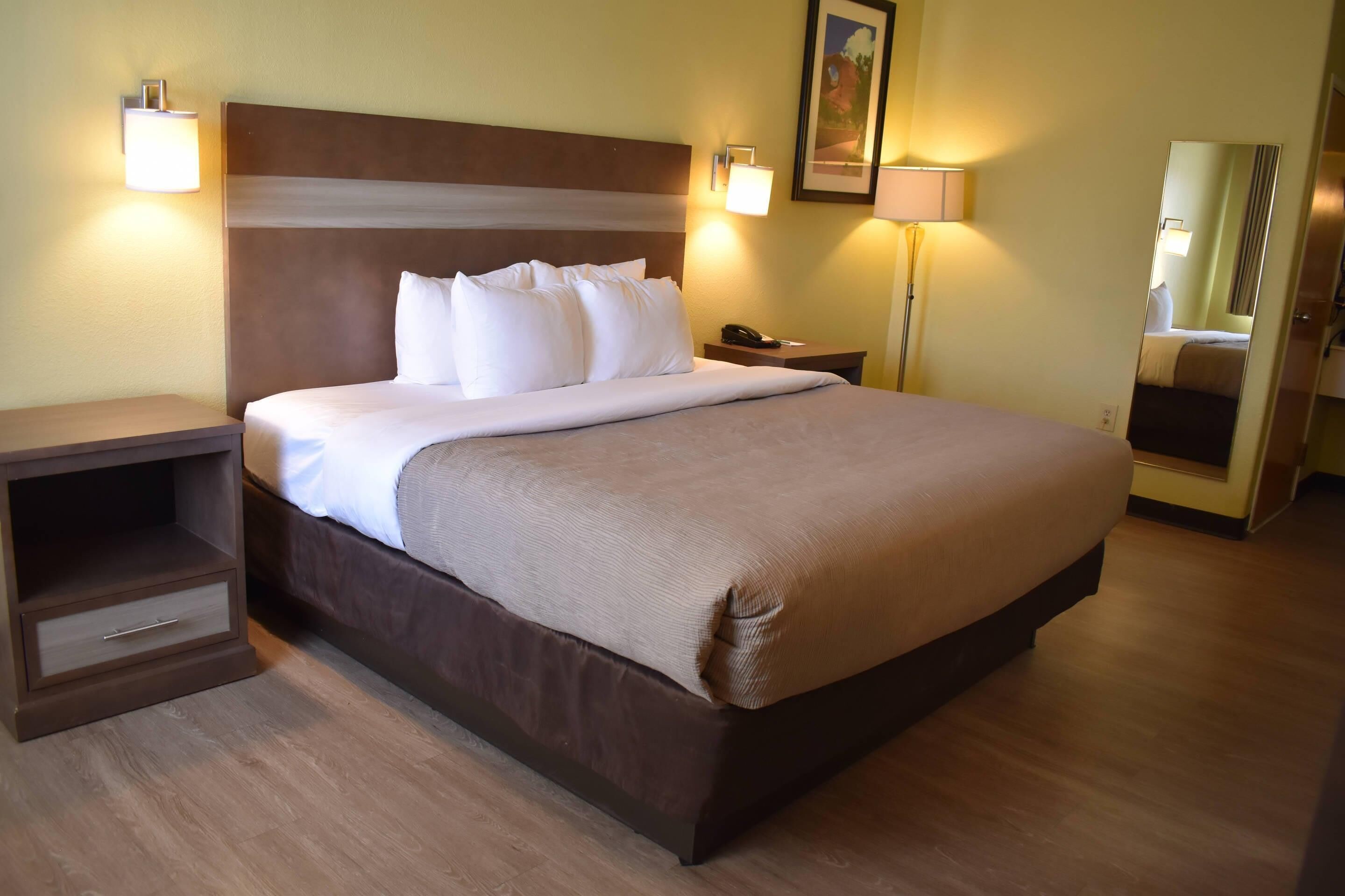 A hotel room with a large bed, bedside tables, a nightstand, a lamp, and a mirror.