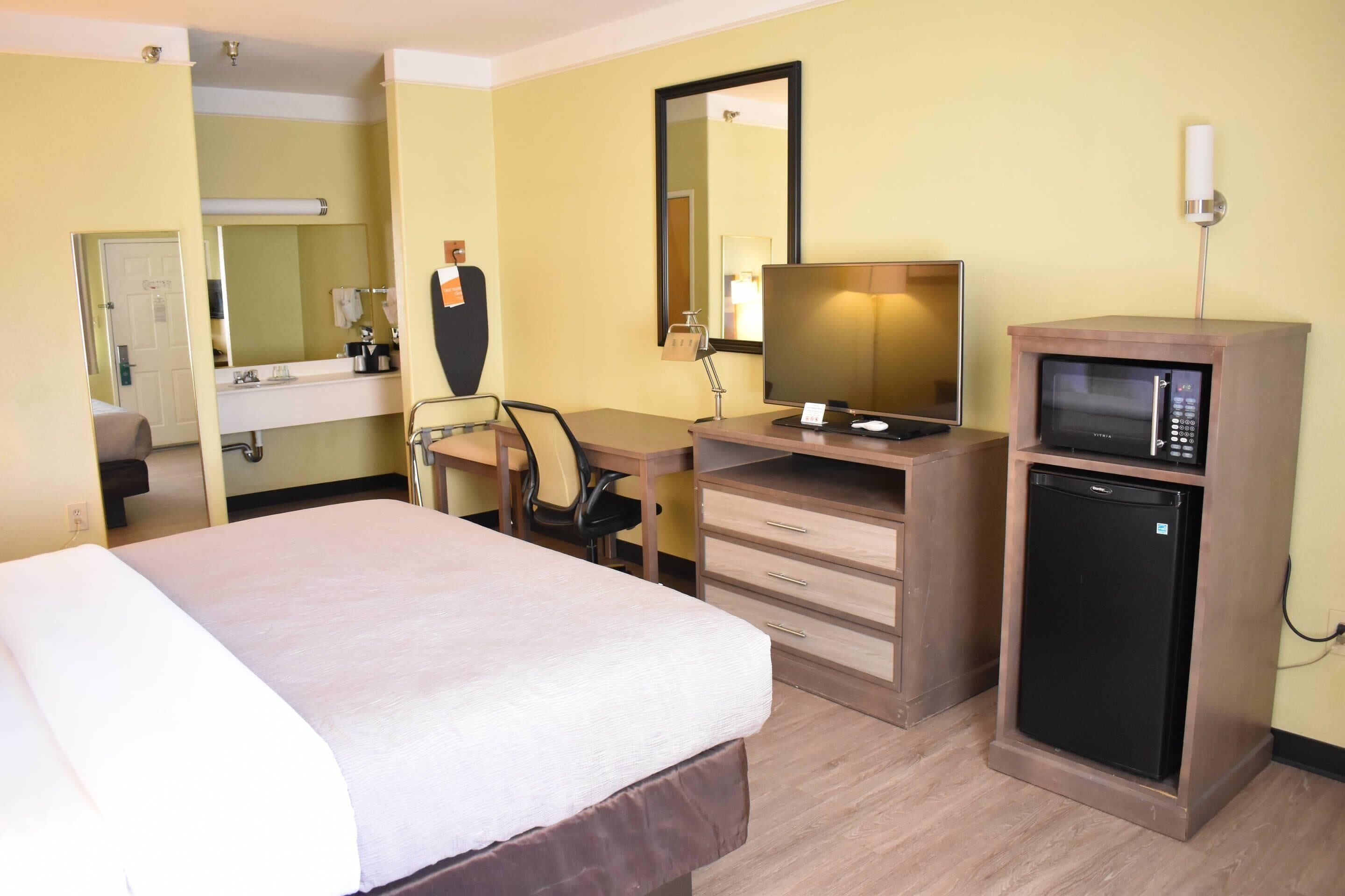 Una habitación de hotel con una cama, un escritorio con computadora, un microondas, una silla y un espejo.