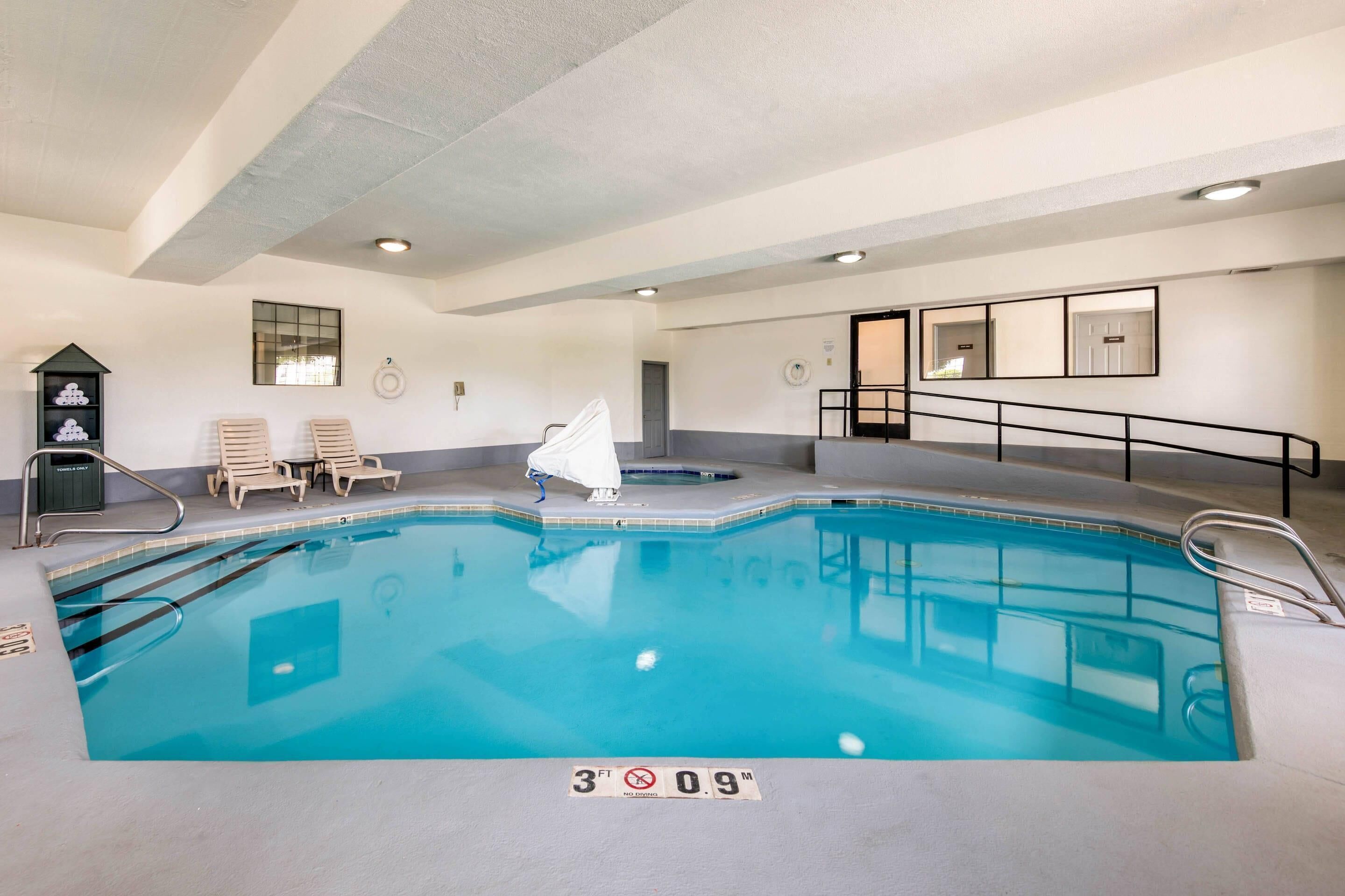 An indoor swimming pool with a 3 FT 9 IN depth marker, lounge chairs, and a small hot tub.