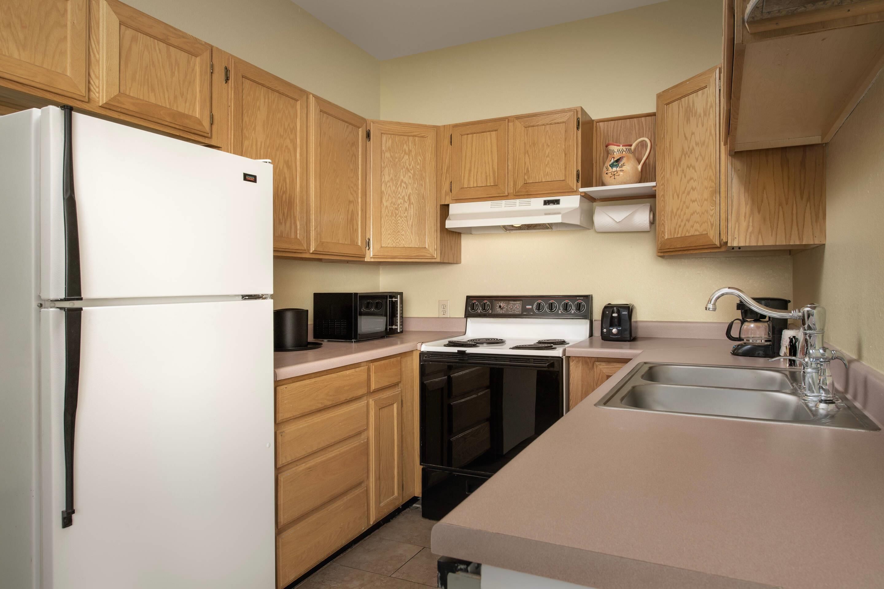A kitchen with wooden cabinets, a white refrigerator, a microwave, an oven, and a sink.