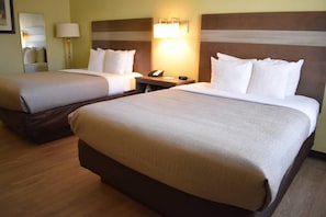 A hotel room with two beds, a nightstand, a lamp, and a mirror.