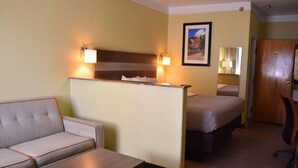 A hotel room with a sofa, a desk, a bed, a nightstand, and a wall-mounted lamp. - Quality Inn & Suites Gallup I-40 Exit 20 (Gallup)