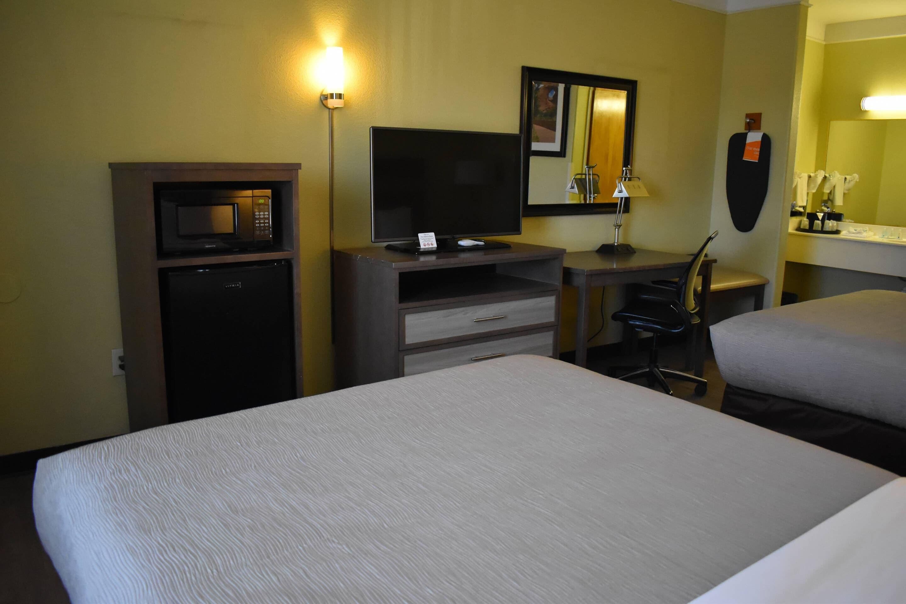 Habitación de hotel con cama, escritorio con televisor, microondas, silla y refrigerador pequeño.