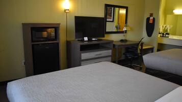 Habitación de hotel con cama, escritorio con televisor, microondas, silla y refrigerador pequeño.