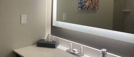 A bathroom with a white sink, a mirror, and a towel dispenser.