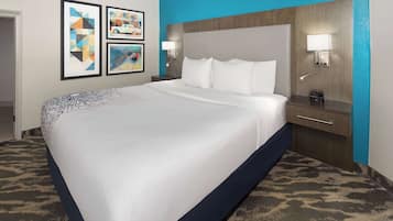 A hotel room with a large bed, a wooden headboard, two bedside tables with lamps, and a carpeted floor.