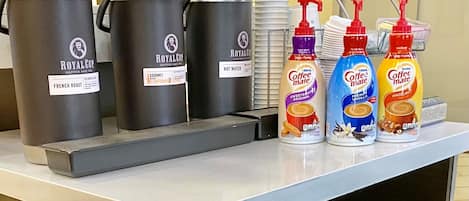 A coffee station with multiple Royal Cup coffee and tea dispensers, a hot water dispenser, and three Coffee Mate bottles with different flavors.