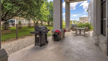 An outdoor patio with a grill, seating area, and a view of a building in the background.