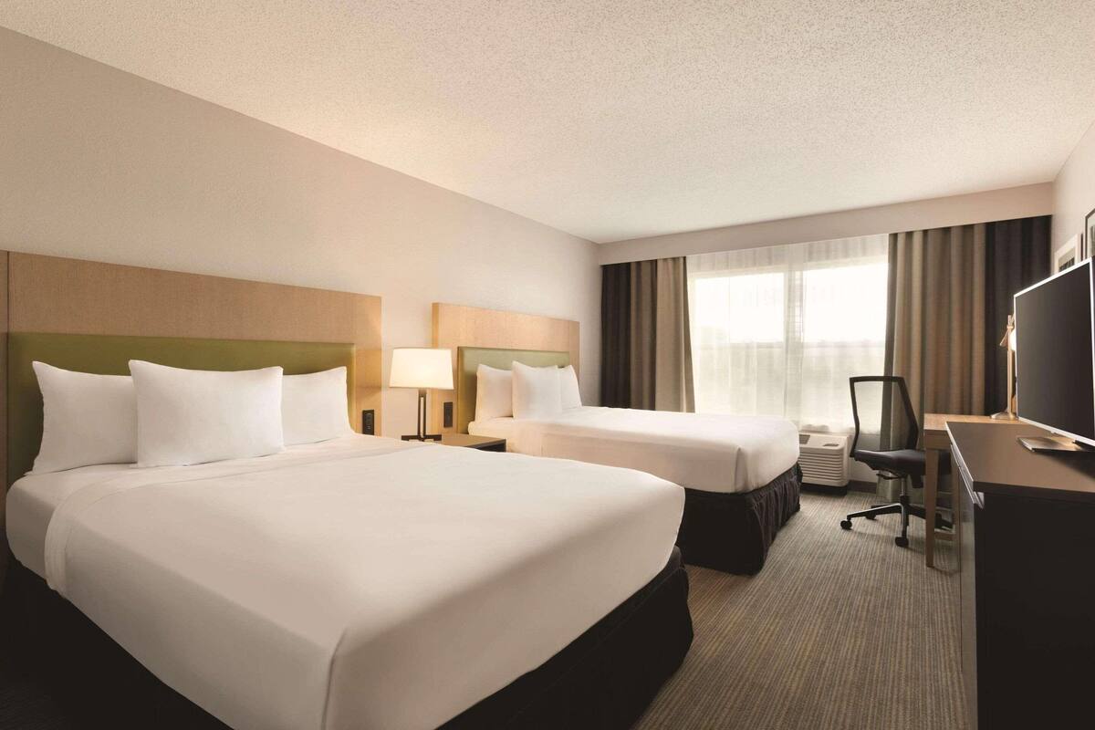 A hotel room with two beds, a desk, a chair, and a television.