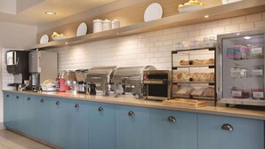 Une cuisine professionnelle dotée d’un comptoir bleu, d’appareils électroménagers en acier inoxydable et d’une vitrine réfrigérée où sont exposés des produits alimentaires.