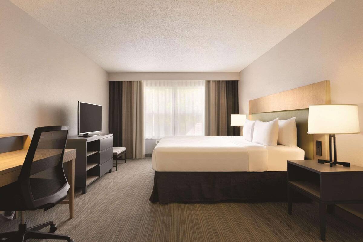 A hotel room with a bed, a desk with a chair, a television, and a lamp.