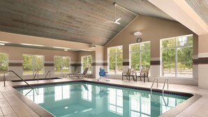 Une piscine intérieure à l’eau d’un bleu cristallin, entourée de chaises longues et dotée d’un ventilateur de plafond.