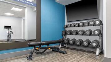 A gym with a bench, dumbbells, a stationary bike, and a mirror.
