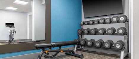 A gym with a bench, dumbbells, a stationary bike, and a mirror.