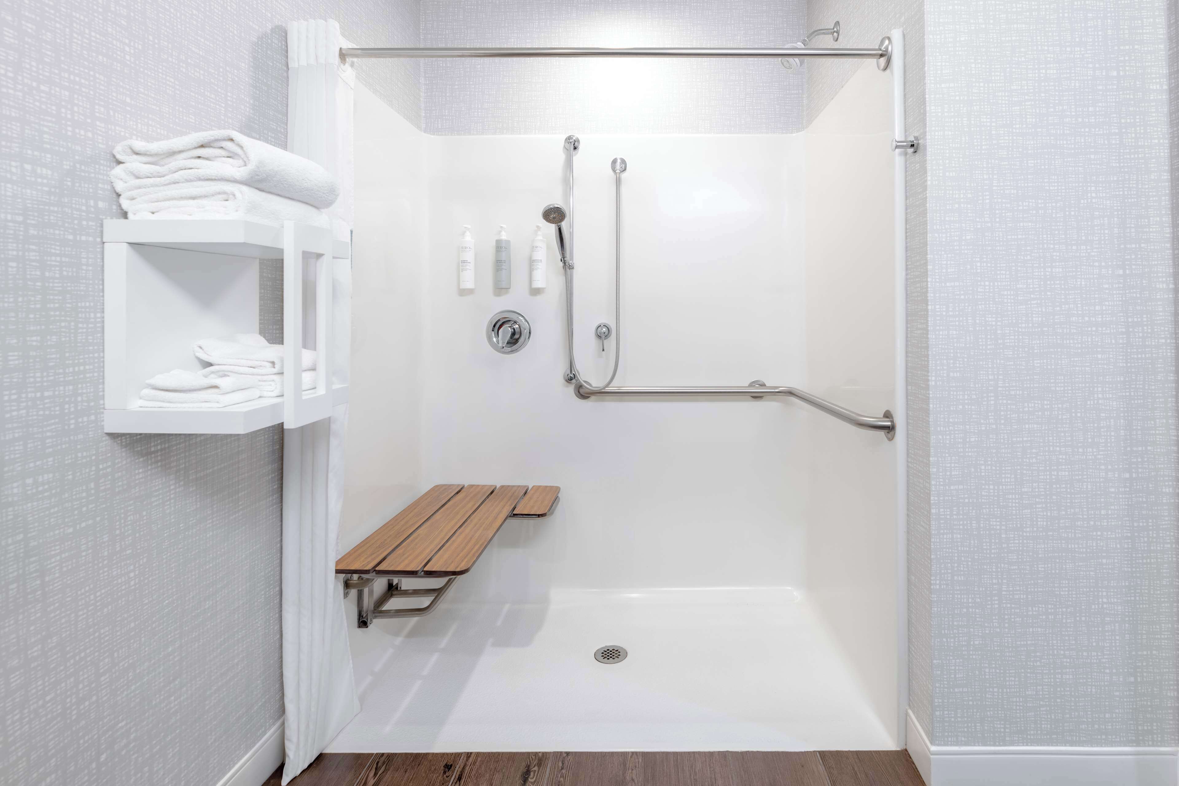 A walk-in shower with a bench, a shelf with towels, and a handrail.