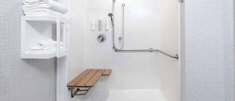 A walk-in shower with a bench, a shelf with towels, and a handrail.