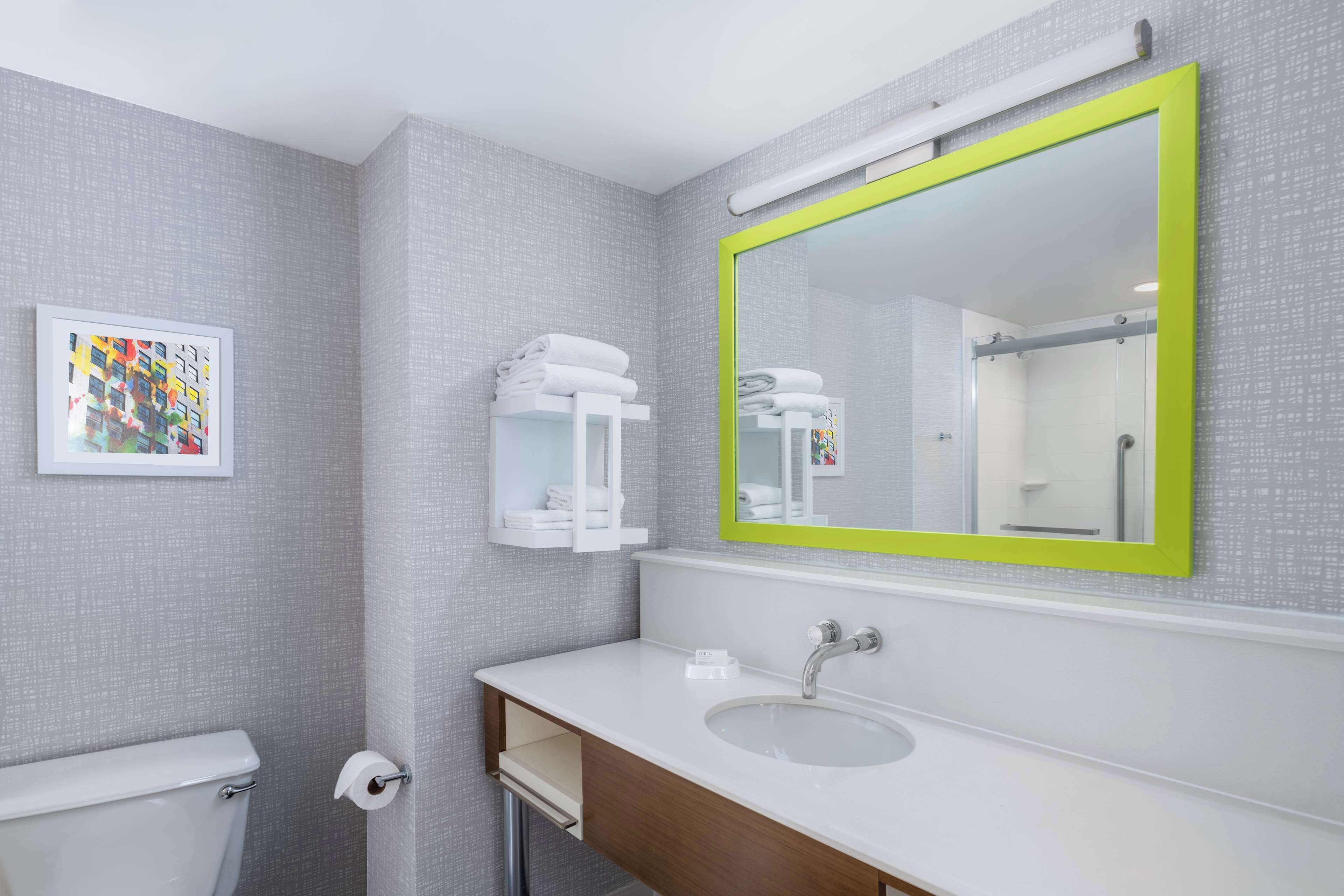 Un baño con lavamanos blanco, un espejo con marco verde, inodoro y un perchero para toallas.