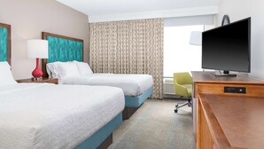 A hotel room with two beds, a television, a desk, and a chair.
