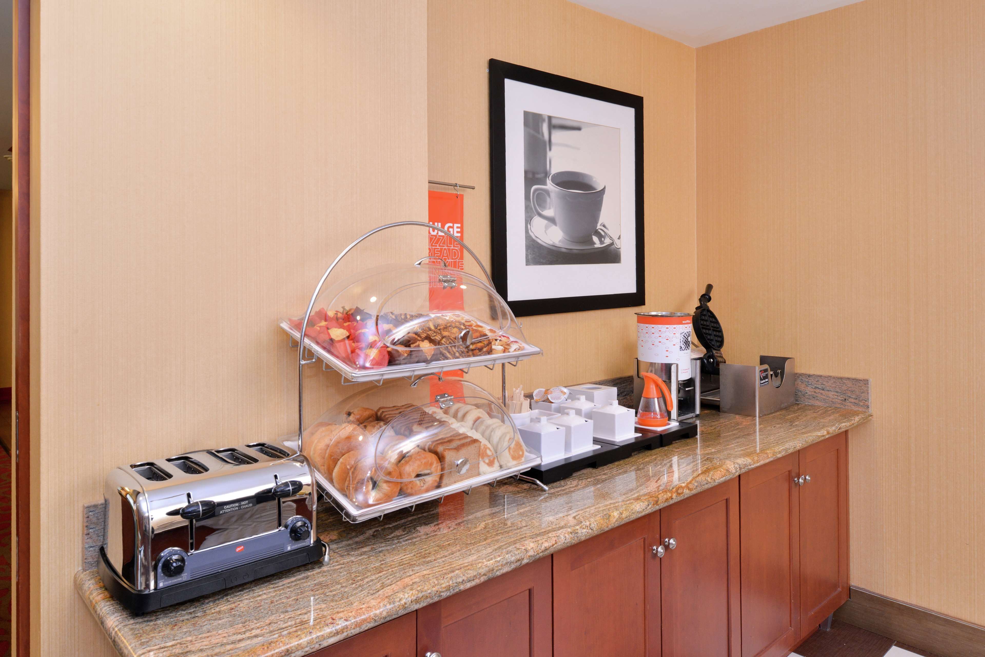 A breakfast station with a toaster, a bread display, a coffee maker, and a framed picture on the wall.