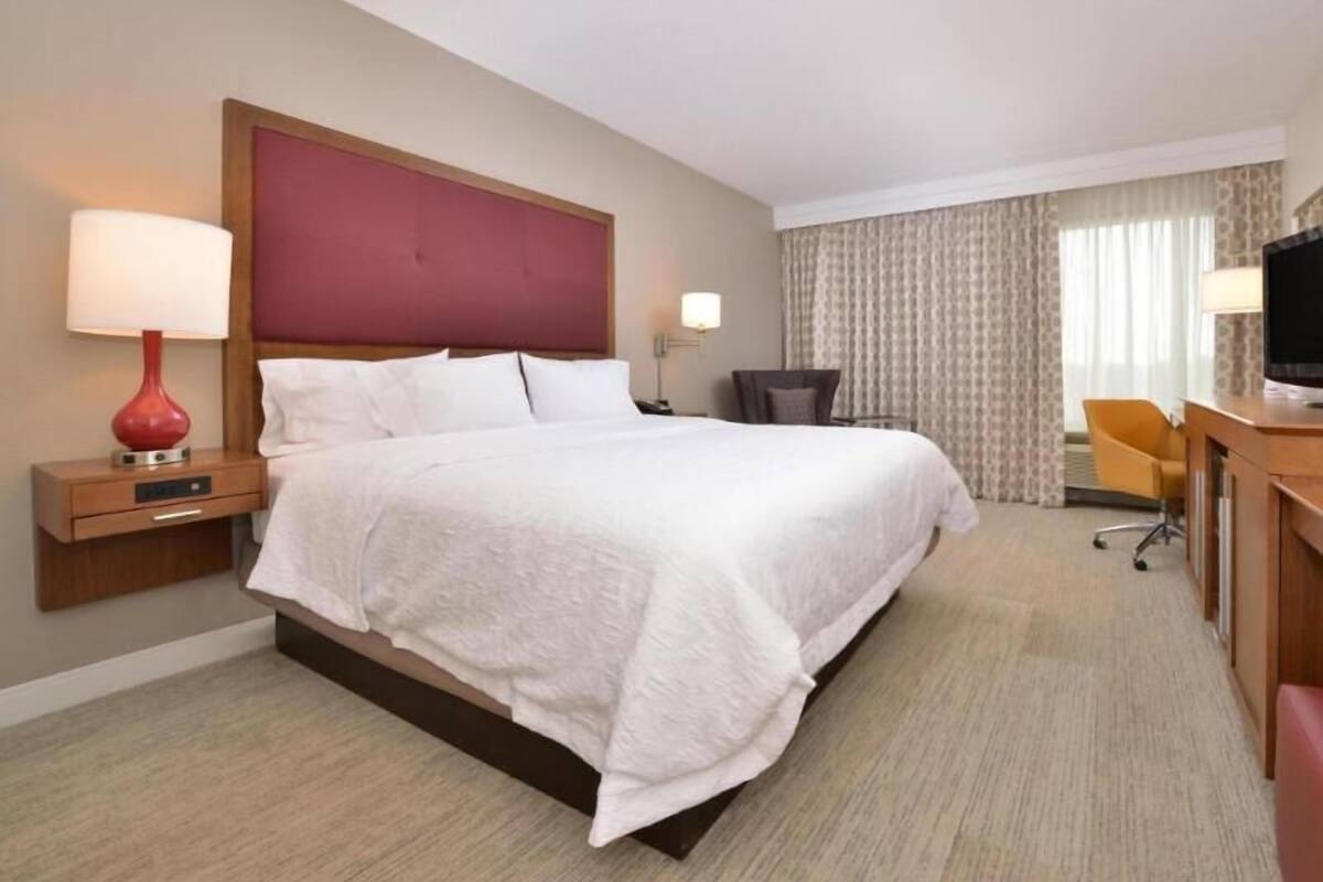A hotel room with a bed, bedside tables, a desk, a chair, and a television.