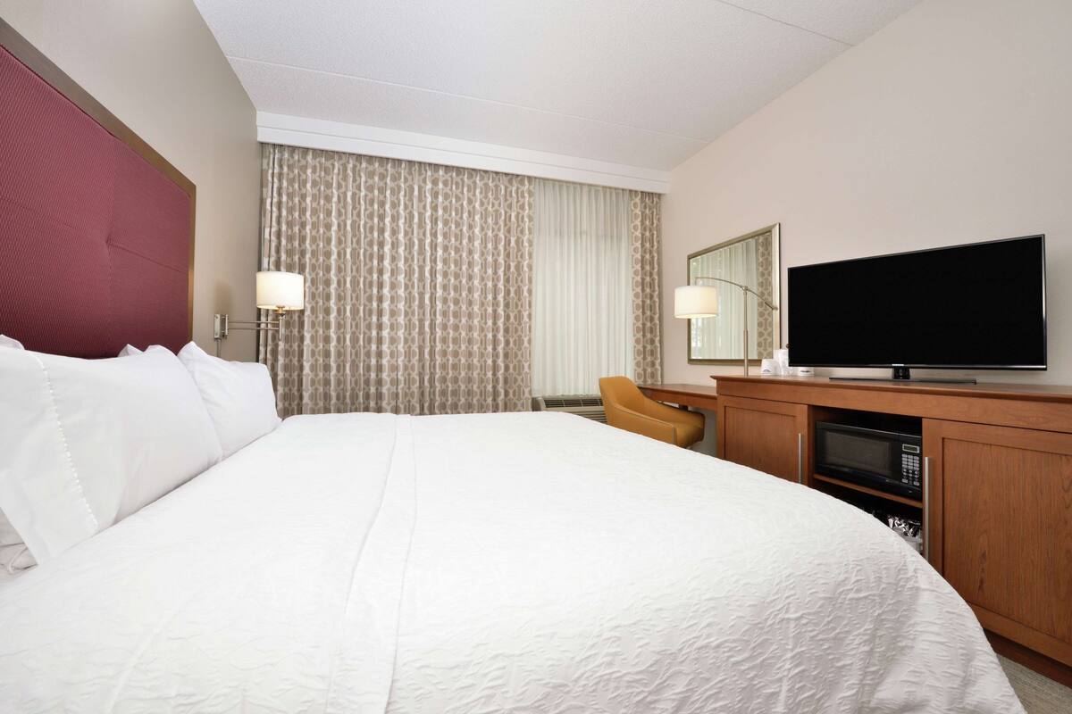A hotel room with a large bed, a television, a desk with a chair, and a microwave.