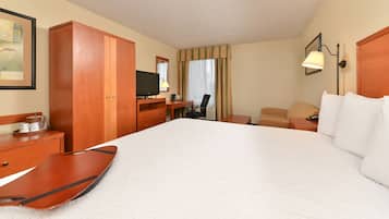 A hotel room with a large bed, wooden wardrobe, desk with a chair, a television, and a lamp.