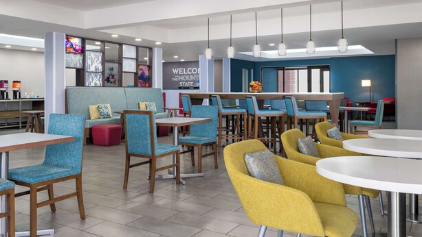 A modern hotel lobby with seating areas, a reception desk, and a 'Welcome' sign.