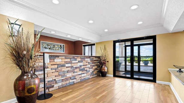 A reception area with a stone wall, wooden flooring, and a large vase with dried plants. - Best Western Inn (Clanton)