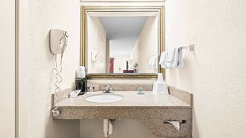 A bathroom with a granite countertop sink, a mirror with a gold frame, a hairdryer, and a towel rack.
