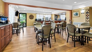 A dining area with multiple tables and chairs, a kitchen area with appliances, and a view of the outdoors. - Best Western Inn (Clanton)