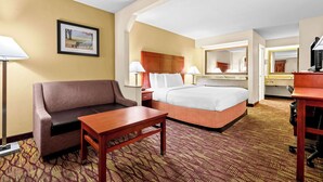 A hotel room with a bed, a sofa, a desk, a lamp, and a framed picture on the wall. - Best Western Inn (Clanton)