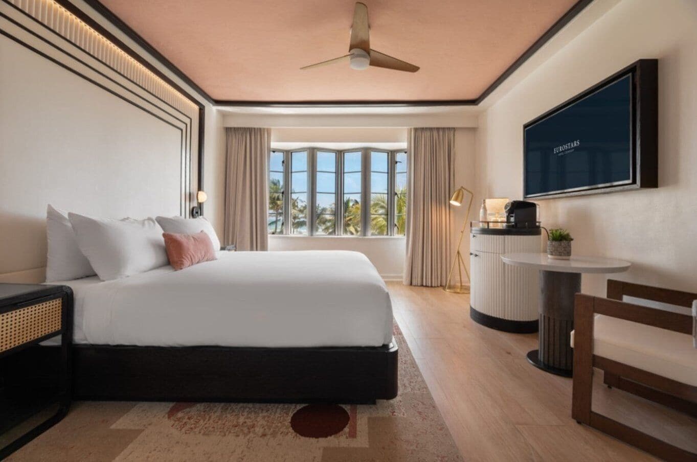 Habitación de hotel con cama, escritorio, silla, televisor y vistas al exterior.