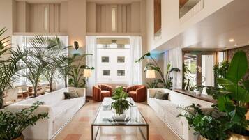 A spacious lobby with a central coffee table, seating area with sofas, and potted plants.