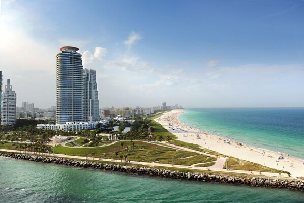A coastal cityscape with a prominent hotel featuring a curved design, a beachfront, and a rocky breakwater. - Eurostars Winter Haven (Miami Beach)