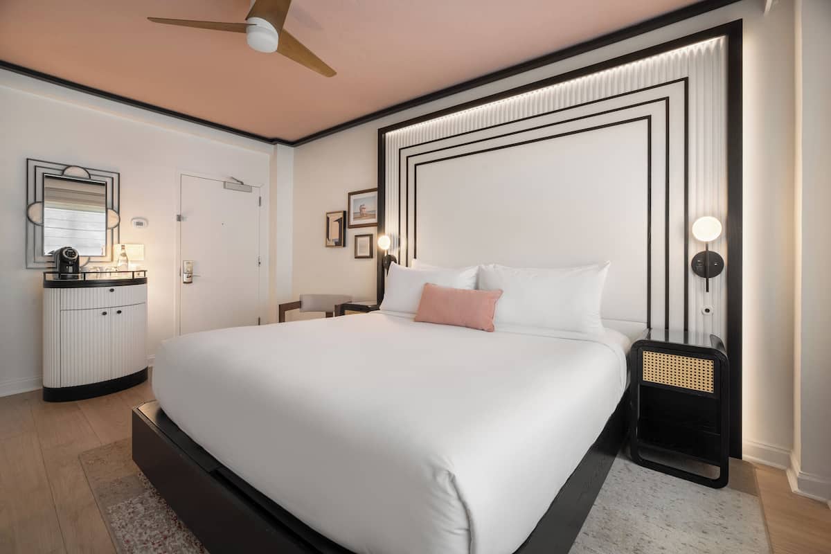 A modern bedroom with a large bed, bedside tables, a ceiling fan, and a nightstand with a lamp.