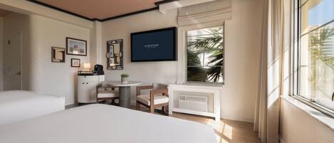 A hotel room with a bed, a small table with chairs, a TV on the wall, and a window with curtains.