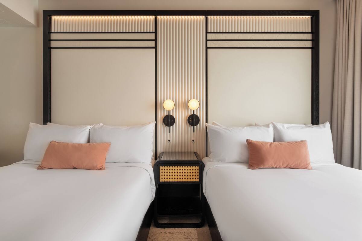 A hotel room with two beds, a nightstand, and a wall-mounted light fixture.